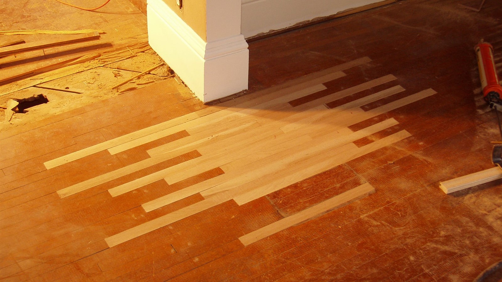 New oak boards laced into a damaged hardwood floor during a repair, blending into the original floor around them