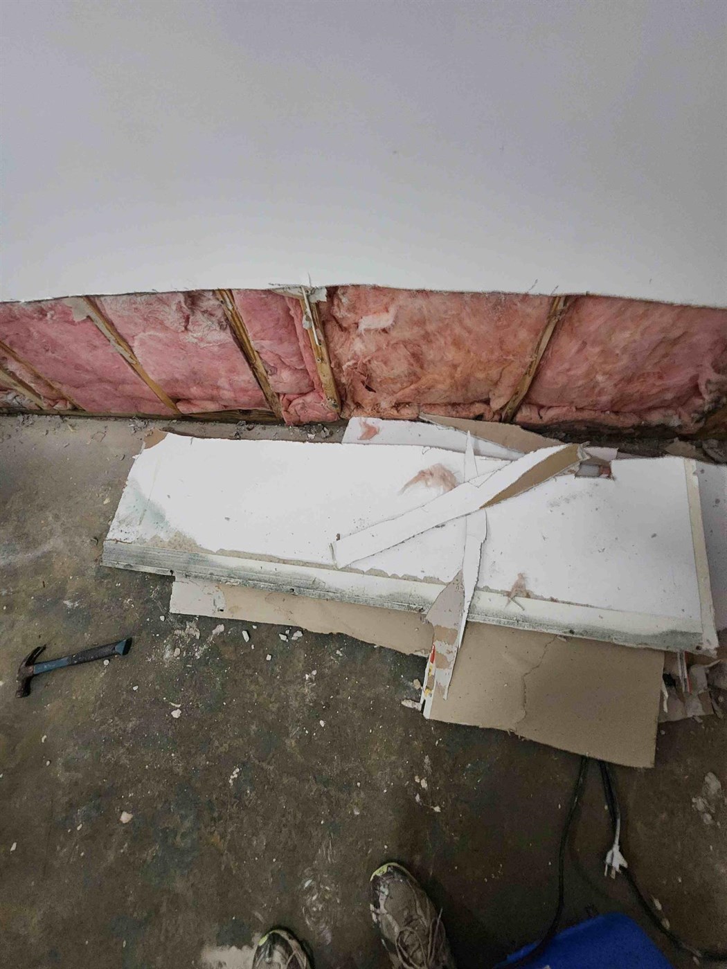 A wall opened up during a water damage job, with wet drywall cut away to expose the studs and pink insulation behind it, and the removed boards stacked on the floor